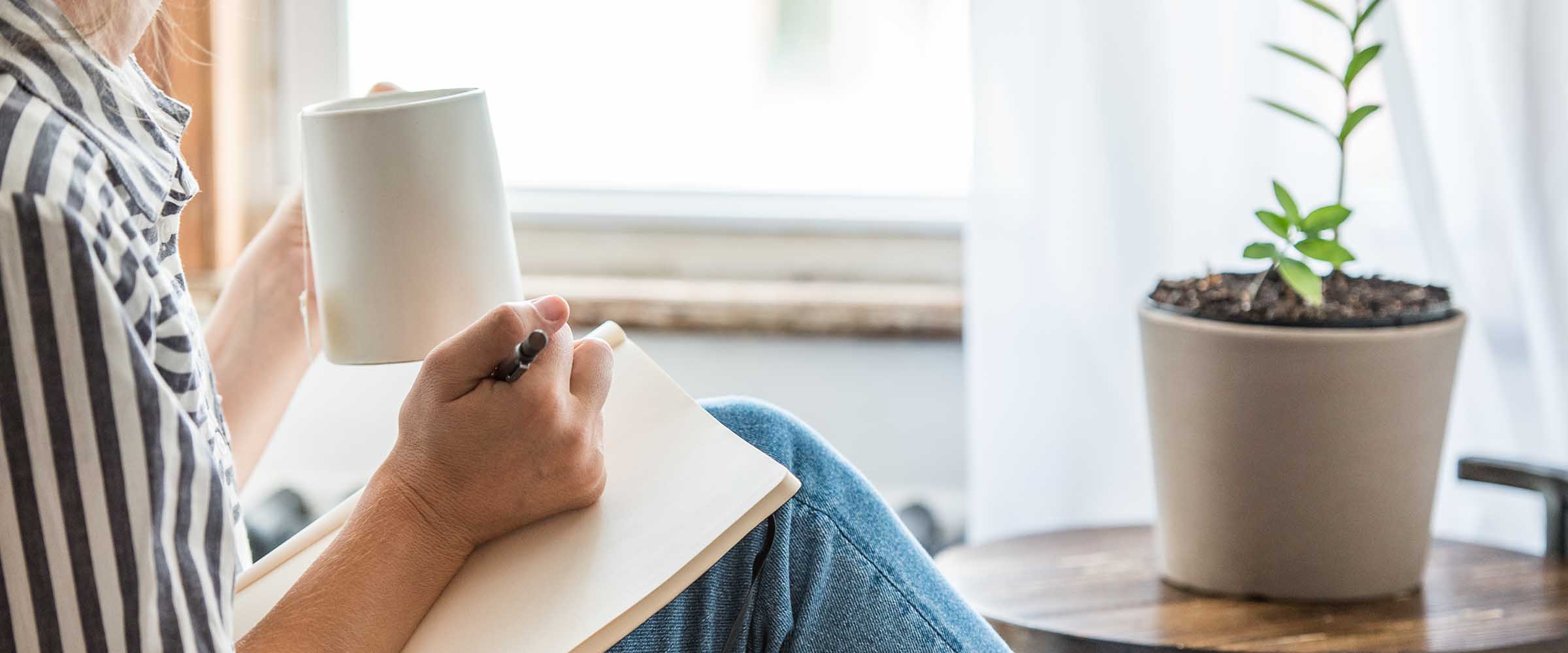 Close up of an educator drinking cup of coffee while writing in a notebook.