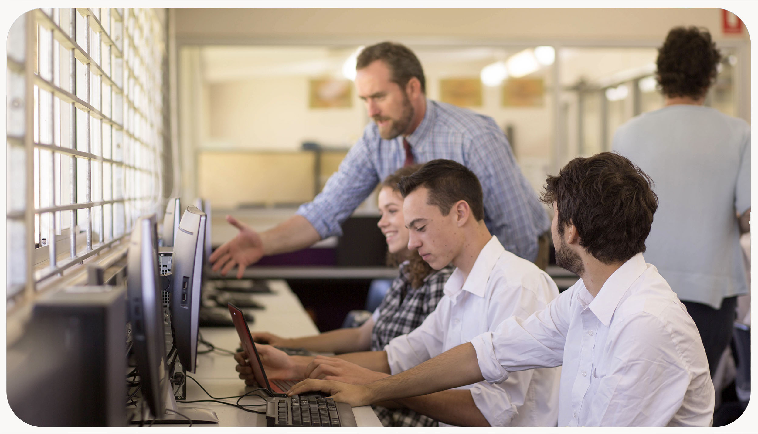 Adolescents working at computers, with an educator assisting